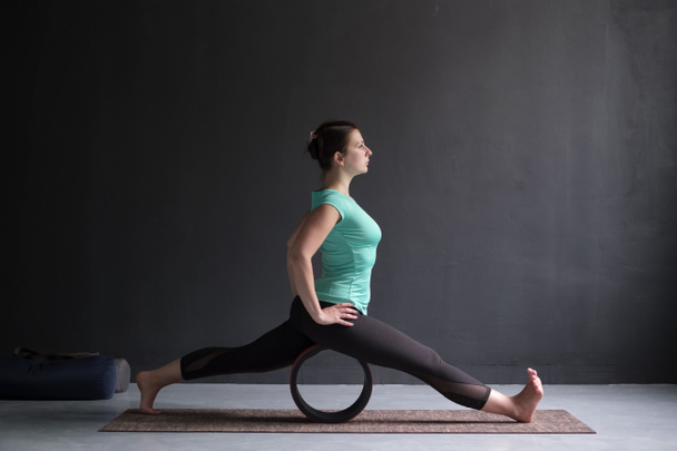 Mujer joven haciendo yoga o ejercicios de pilates. Escisiones, hanumanasana usando rueda
 - Foto, Imagen