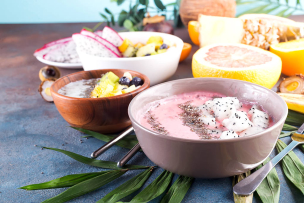 red or pink smoothie acai bowls topped with fresh pitaya and chia seeds on palm leaf on stone background, - Photo, Image