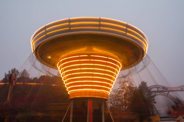 Un carrousel de chaîne coloré flou en mouvement au parc d'attractions, illumination du soir. L'effet du bokeh et de l'exposition prolongée
 - Photo, image
