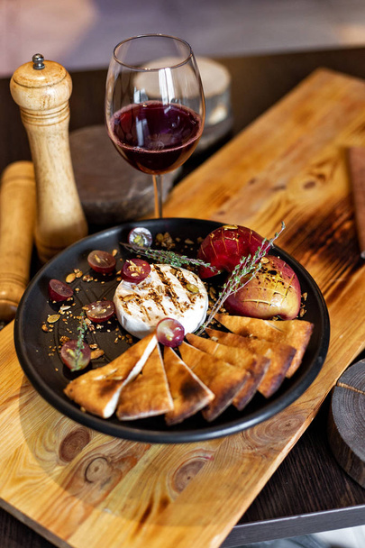 Grilled camembert with baked apple and grapes with slices of bread, served on a black plate on a wooden background in rustic style. Restaurant serving - Foto, afbeelding