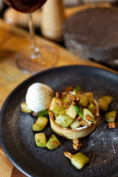 English apple crumble with nuts, mint and scoop of ice cream served on a black plate on a wooden background in rustic style. Restaurant serving - Zdjęcie, obraz