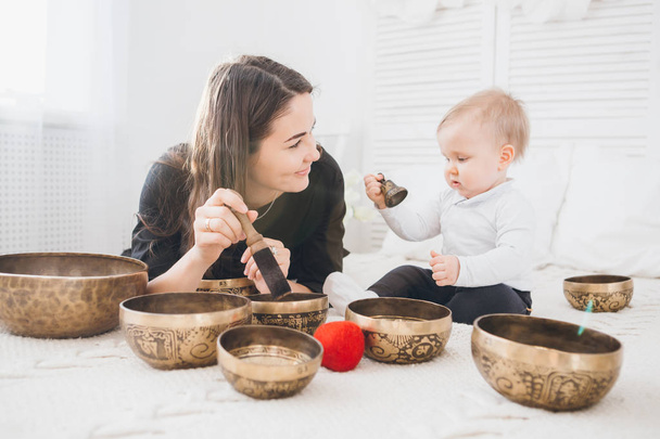 Little boy playing with Tibetan singing bowls sitting on the bed. Sound therapy for the baby. Toning. - Φωτογραφία, εικόνα