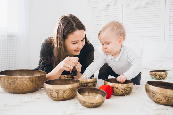 Little boy playing with Tibetan singing bowls sitting on the bed. Sound therapy for the baby. Toning. - Foto, imagen