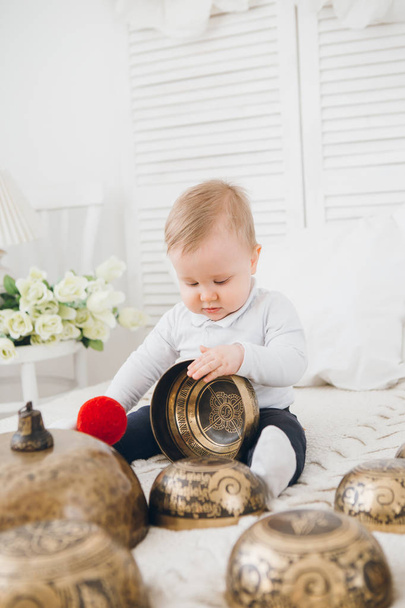 Little boy playing with Tibetan singing bowls sitting on the bed. Sound therapy for the baby. Toning. - Photo, Image