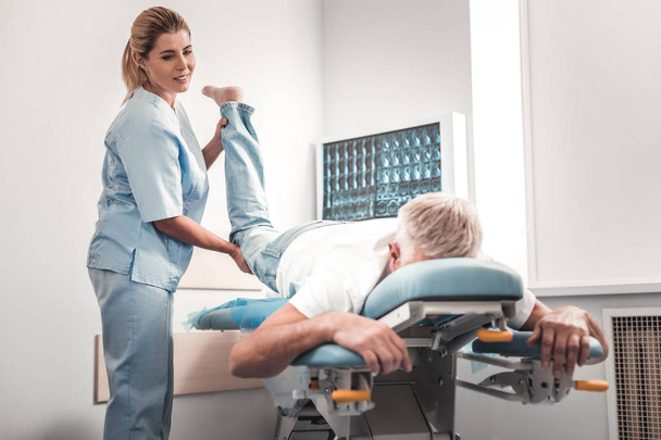 Chiropractor in blue uniform checking legs of elderly man - Foto, afbeelding