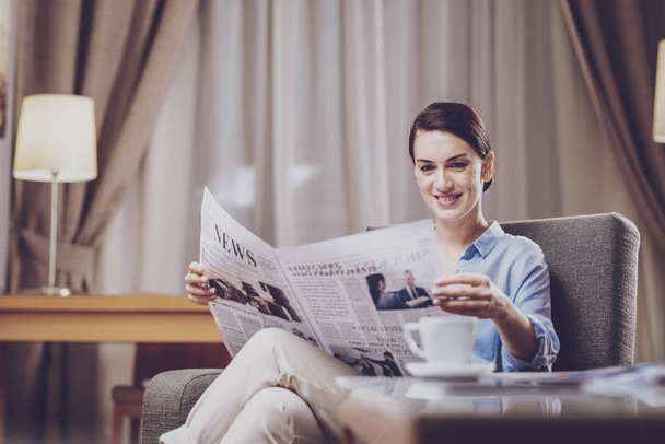 News announcement. Pleasant positive businesswoman having attractive appearance and spending time at home while enthusiastically reading articles in the newspaper - 写真・画像