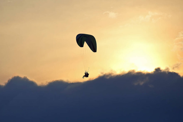 Paraglider flying on a wing in the sky against the setting sun - Photo, image