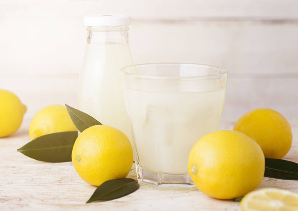 Glass and bottle of organic fresh lemon juice with raw lemons on light wooden background - Photo, Image