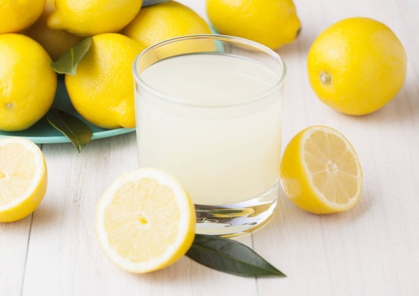 Glass of organic fresh lemon juice with raw lemons on light wooden background - Φωτογραφία, εικόνα