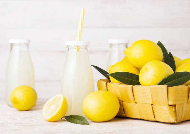 Glass bottles of organic fresh lemon juice with raw lemons in bamboo basket on wooden background - Foto, afbeelding