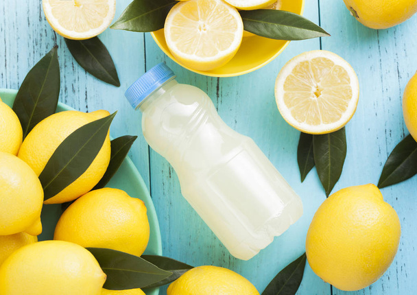 Plastic bottle of organic fresh lemon juice with raw lemons on blue wooden background.Top view - Fotografie, Obrázek