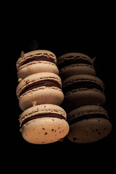 Reihe von drei Erdnussmakronen mit Schokoladenfüllung serviert auf schwarzem Spiegelhintergrund mit Spiegelung - Foto, Bild
