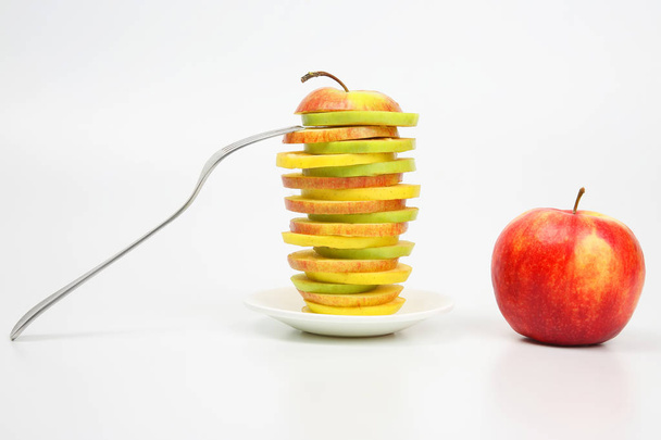Apple cut into pieces on a white saucer with a fork - 写真・画像