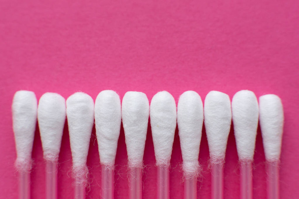 Closeup view from above on heads of cotton buds laid in a horizontal line on pink background. - Photo, image