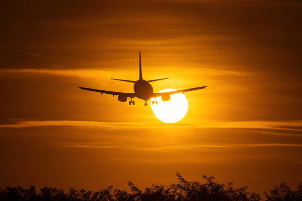 Silhouet van een vliegtuig over de zon met prachtige rode wolken in de achtergrond - Foto, afbeelding