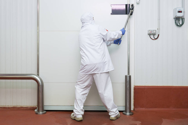 trabajador de la sala de corte de carne manipulando una puerta corredera de la cámara del refrigerador
 - Foto, imagen