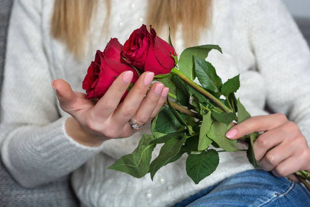 Молода жінка тримає красиві червоні троянди в руках і сидячи в ліжку у себе вдома. Жінка день і концепція день Святого Валентина. Крупним планом, вибіркове фокус - Фото, зображення