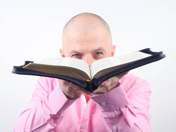 ο άνθρωπος σε ένα ροζ πουκάμισο με μια ανοικτή Αγία Γραφή στα χέρια του - Φωτογραφία, εικόνα