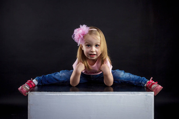 Portrait of cute European little blonde girls in jeans and pink t-shirt with the inscription: "Dad's pride, mom's joy", on a black isolated background - Foto, Imagem