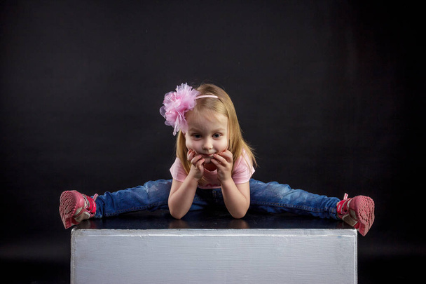 Portrait of cute European little blonde girls in jeans and pink t-shirt with the inscription: "Dad's pride, mom's joy", on a black isolated background - Foto, Imagem