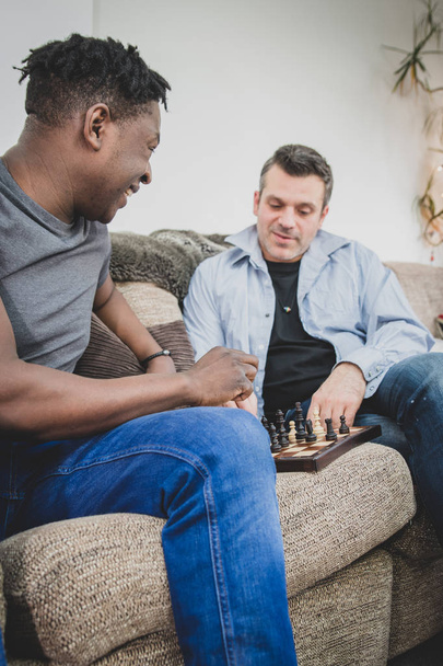 Ένα γκέι ζευγάρι, απολαμβάνοντας χρόνο σε εσωτερικούς χώρους στο σπίτι, να παίζει σκάκι.  - Φωτογραφία, εικόνα