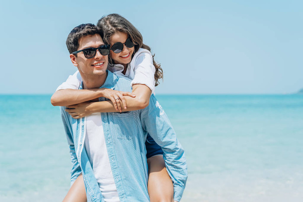 Пара влюбленных - Красивый мужчина несет свою улыбающуюся девушку на спине под голубым небом на пляже
 - Фото, изображение