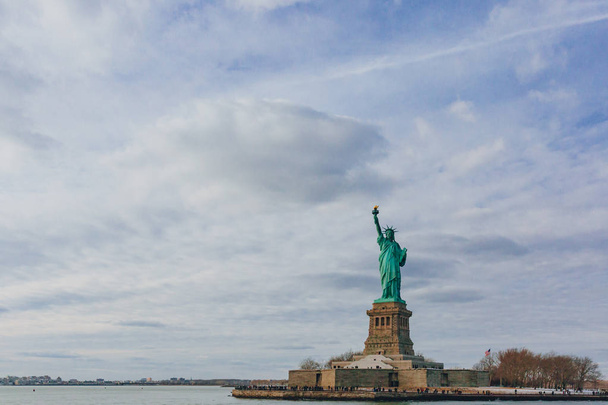 Blick auf die Freiheitsstatue mit Blick auf Wasser unter Himmel und Wolken, in New York City, USA - Foto, Bild