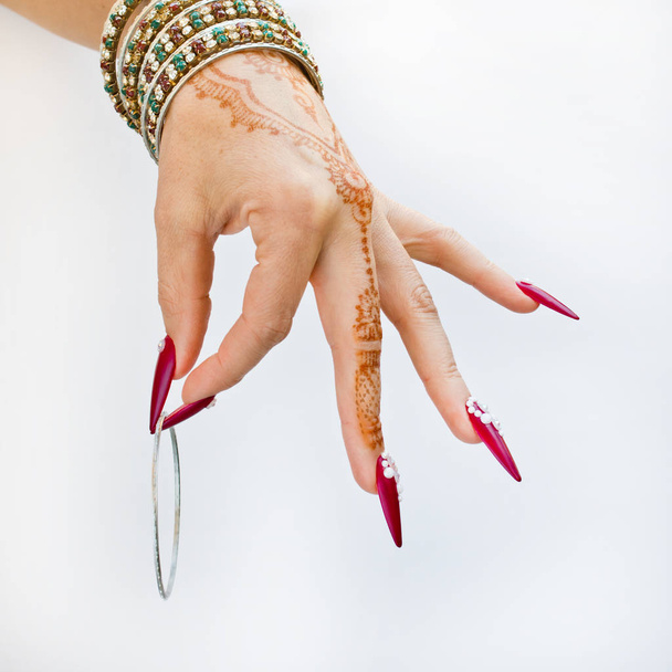 hand met henna tattoo, nagels versierd met brilliants en armbanden met edelstenen - Foto, afbeelding