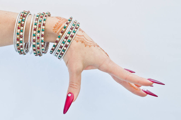 hand met henna tattoo, nagels versierd met brilliants en armbanden met edelstenen - Foto, afbeelding