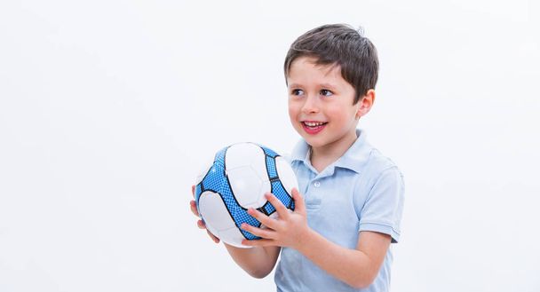 Chlapec s fotbalovým míčem, izolované na bílém studio pozadí. Portrét kid fotbalový hráč s míčem v ruce. Mladý roztomilý pes drží sportovní vybavení. Vzdělávání ilustrační obrázek. - Fotografie, Obrázek