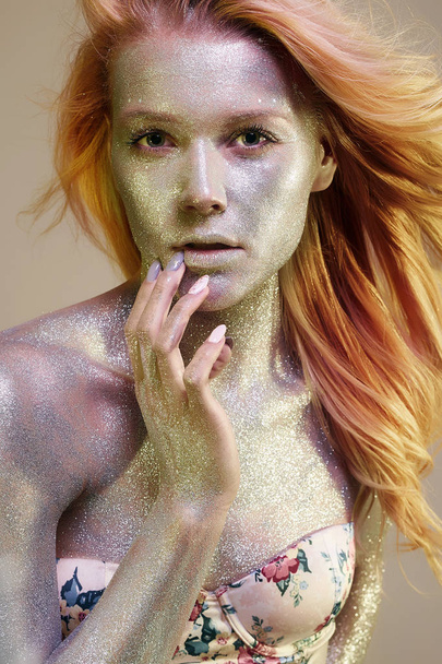 Golden Girl. Mooie jonge vrouw met Sparkles op haar gezicht en lichaam. Art Make-Up, in kleurrijk licht - Foto, afbeelding