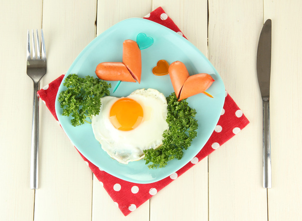 Sausages in form of hearts, scrambled eggs and parsley, on color plate, on wooden background - Φωτογραφία, εικόνα