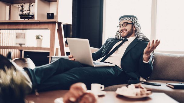 Businessman Using Laptop. Arab Businessman. Man Wearing in Black Suit. Experienced Entrepreneur. Successful Young Man. Work in Office. Arab in glasses. communicate by video link. lying on couch. - Zdjęcie, obraz