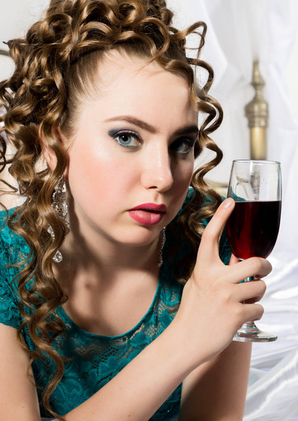 mysterious young curly woman resting on the bed and drinks red wine - Photo, Image