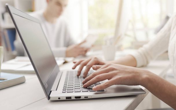 Жінка використовує ноутбук і з'єднується, інший студент сидить за столом на задньому плані, руки крупним планом
 - Фото, зображення