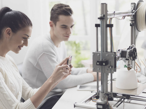 Engineering students printing prototype models using a 3D printer, the girl is taking pictures with a smartphone and sharing online - Zdjęcie, obraz