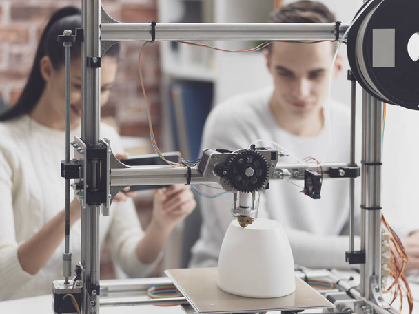 Engineering students printing prototype models using a 3D printer, the girl is taking pictures with a smartphone and sharing online - Fotografie, Obrázek
