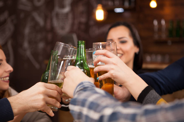 Szczęśliwy, młodzi przyjaciele, brzęk butelek piwa w starodawny stary pub stylu - Zdjęcie, obraz