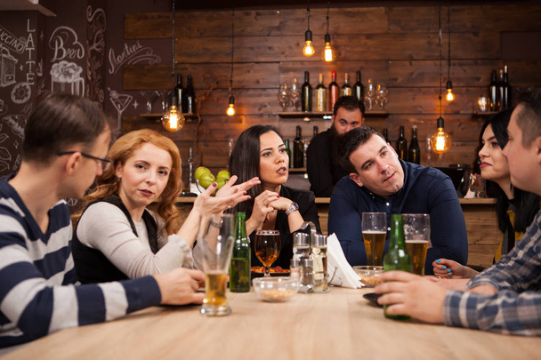 Grupo de jovens amigos sentados à mesa no bar juntos
 - Foto, Imagem