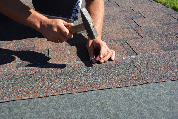 Construção de telhados. Roofer instalação de telhas de asfalto na construção da casa canto do telhado com martelo e unhas
.   - Foto, Imagem