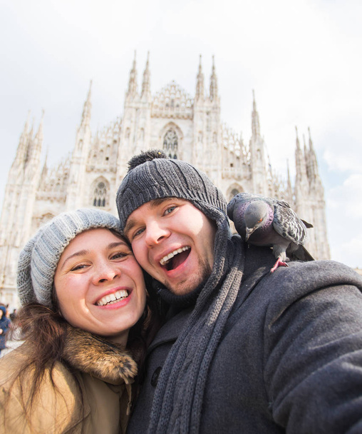 Viajes de invierno y concepto de vacaciones - Felices turistas tomando un autorretrato con divertidas palomas frente a la catedral del Duomo en Milán
 - Foto, Imagen