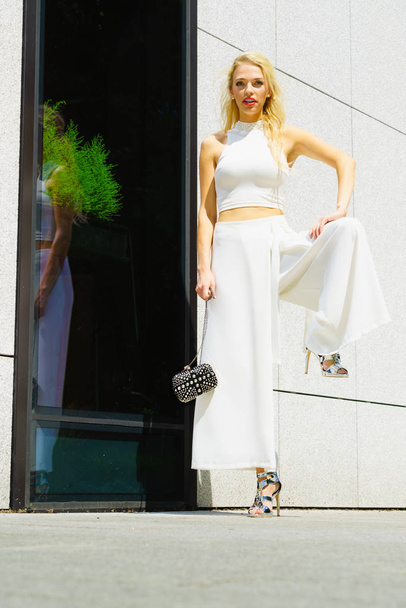 Elegant fashionable woman presenting trendy urban outfit. White crop top and trousers culottes. Outdoor photo session, unusual bizarre pose - Фото, изображение