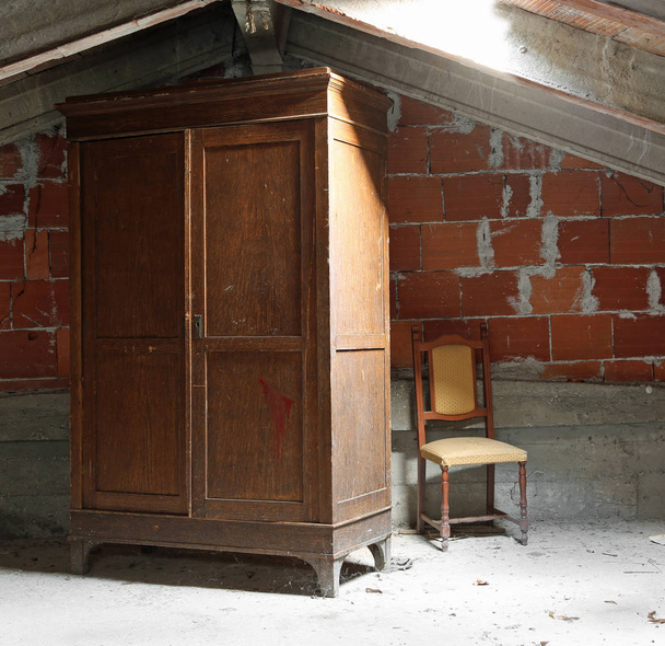 viejo armario de madera y una silla rota en el ático polvoriento con la luz de la claraboya
 - Foto, Imagen