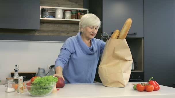 Kobieta emeryt rozpakowaniu foos z torebki sklep spożywczy w kuchni. - Materiał filmowy, wideo