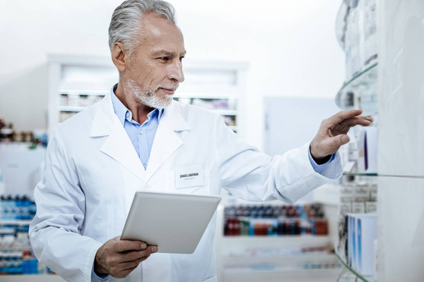 Grey-haired handsome pharmacist in a white coat making notes - Фото, изображение