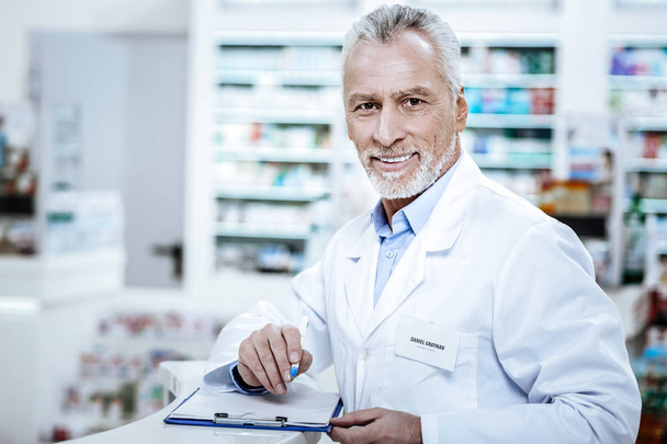 Bearded smiling mature man in a white coat making notes - Foto, imagen