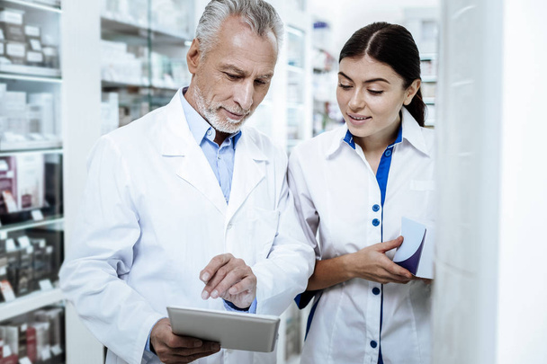 Mature bearded man in a white coat discussing medicines with his young colleague - Foto, Imagen