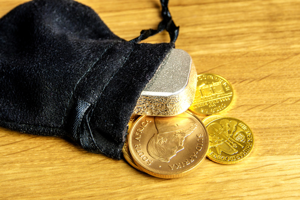 Vértes arany érmék és ezüst tégla esik ki a fekete moneybag, és a tojásrakás fából készült háttér - Fotó, kép