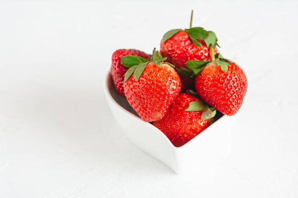 Fresas frescas en un tazón en forma de corazón aislado sobre fondo blanco
. - Foto, Imagen
