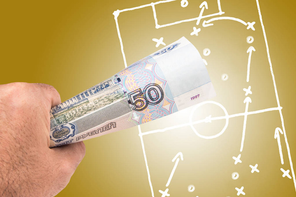 プレイ戦術と金色の背景に描かれた戦略に提出されたサッカー フットボールの画像とロシアのルーブル紙幣を保持している白人男性 - 写真・画像